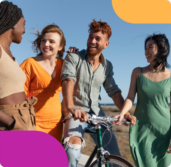 A diverse group of four friends smile and chat as one of them rides a bike under a clear blue sky.