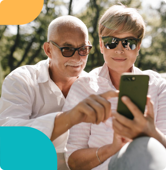 Older couple sitting outdoors, smiling while browsing on a smartphone together.