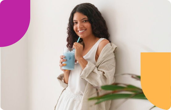 Woman in light clothes sipping a bright blue smoothie and smiling.