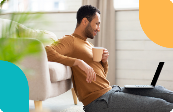 Man sitting on the floor with a coffee, working on a laptop at home.