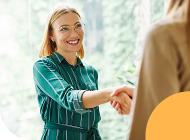 Smiling woman reaching out for a handshake in a light-filled office.